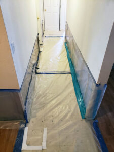 A hallway protected with plastic sheeting and tape, indicating a water damage containment zone by Island Restoration LLC in Kapolei, HI.