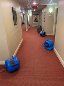 A hallway with multiple air movers and dehumidifiers drying the carpet after water damage by Service Professionals in Edmond, OK.