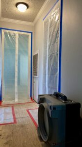 Hallway with plastic containment and a large dehumidifier for water damage remediation by 1st Response Emergency Repairs, LLC in Scott, LA.