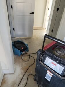Water damage drying equipment, including an air mover and dehumidifier, in a hallway by ABC Cleaning and Restoration in Harvest, AL.
