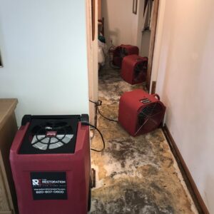 A hallway with multiple industrial drying fans working on a water-damaged floor, part of restoration services by The Restoration Experts in Waupaca, WI.