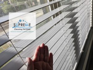 A hand checking freshly cleaned window blinds, demonstrating attention to detail by Supreme Cleaning Services in Farmers Branch, TX.