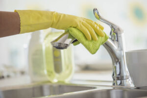 A gloved hand cleaning a kitchen faucet with a green microfiber cloth, provided by Your Green Clean Crew in Bellevue, WA.