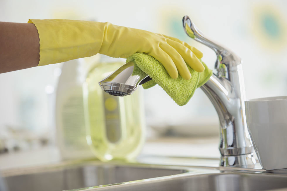 A gloved hand cleaning a kitchen faucet with a green microfiber cloth, provided by Your Green Clean Crew in Bellevue, WA.
