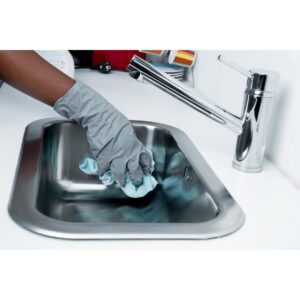 A gloved hand cleaning a stainless steel kitchen sink, a service provided by Harsh's Cleaning Services LLC in Canton, OH.