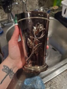A hand cleaning a decorative silver cup over a kitchen sink, part of detailed cleaning by Chelle's Cleaning Services in Gary, IN.