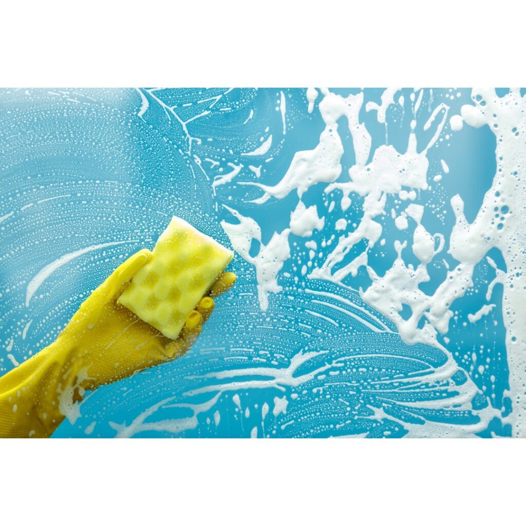 A gloved hand cleaning a window with a sponge and suds, a service offered by Harsh's Cleaning Services LLC in Canton, OH.