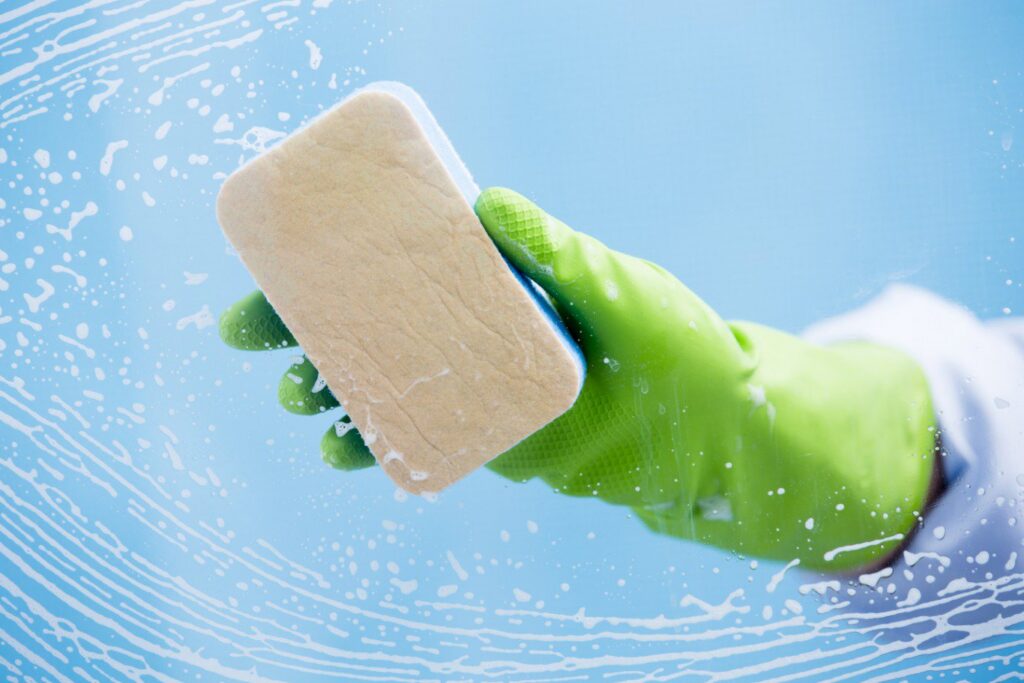 A gloved hand using a sponge to clean a window, leaving suds, representing services by Le Fine Cleaning in South Bend, IN.