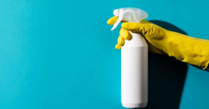 A hand in a yellow cleaning glove holding a white spray bottle, representing professional house cleaning services by Caudle Cleaning LLC in Cincinnati, OH.