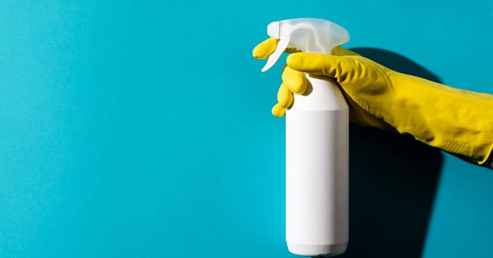 A hand in a yellow cleaning glove holding a white spray bottle, representing professional house cleaning services by Caudle Cleaning LLC in Cincinnati, OH.
