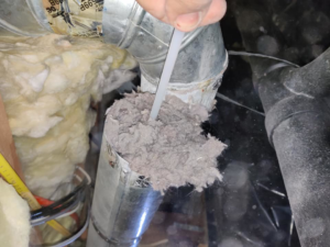 A hand pulling a large clump of lint and dust from a dryer vent, demonstrating a cleaning service by Home Relief Services in Bellevue, WA.