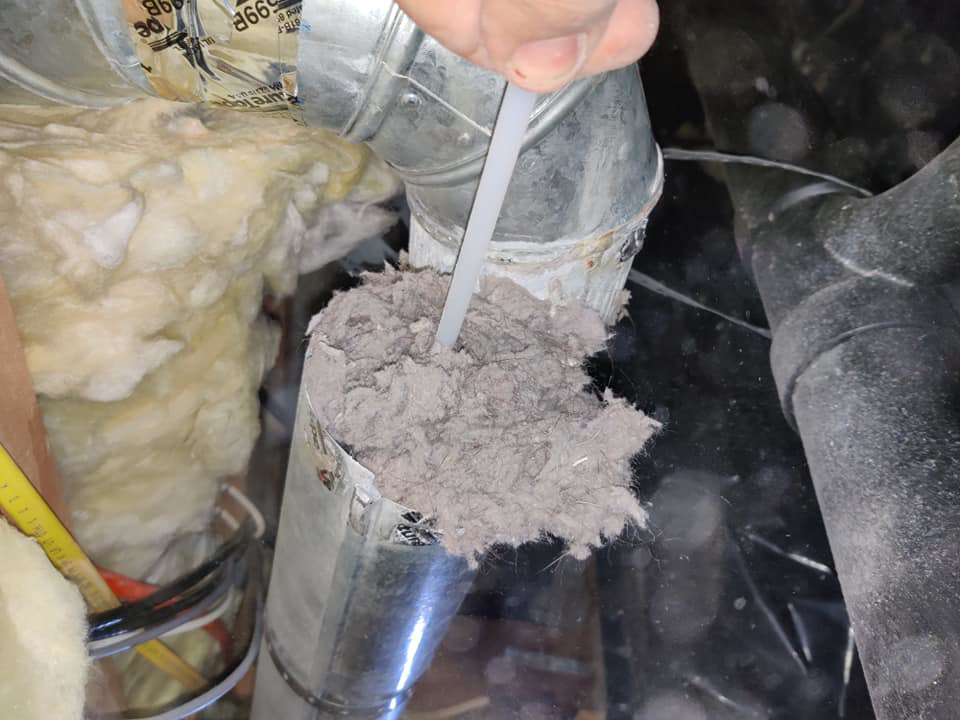 A hand pulling a large clump of lint and dust from a dryer vent, demonstrating a cleaning service by Home Relief Services in Bellevue, WA.
