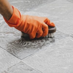 A gloved hand scrubbing floor tiles, showcasing detailed cleaning by Benin Cleaning Services LLC in Orange Park, FL.