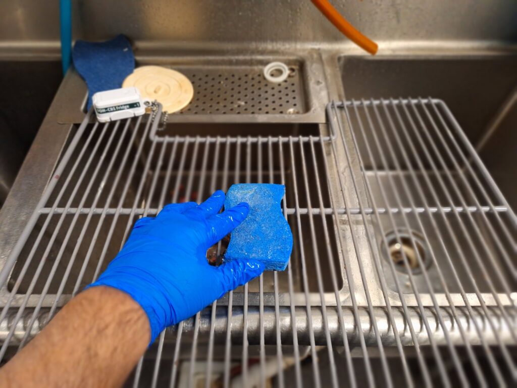 A gloved hand from Absolute Luxury, LLC Residential & Commercial Cleaning scrubs a sink grate in Antioch, TN.