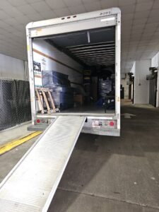 A hand truck in the foreground with a moving truck and ramp in the background, used by Household Goods Moving and Storage in Rockville, MD