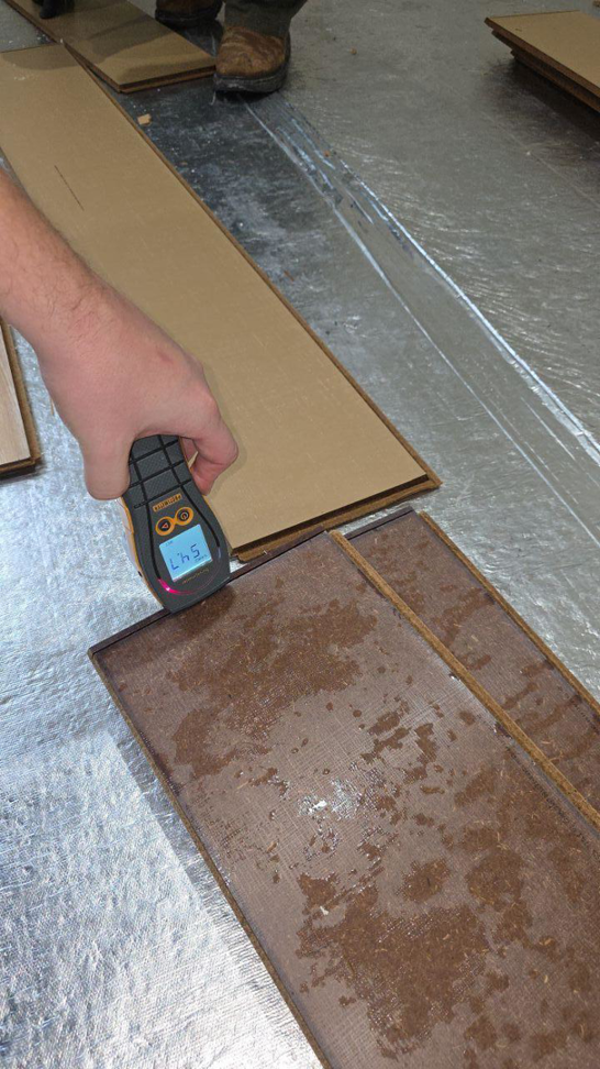 A hand using a moisture meter to check water-damaged flooring at a job site for Restoration Techs, LLC in Oregon City, OR.