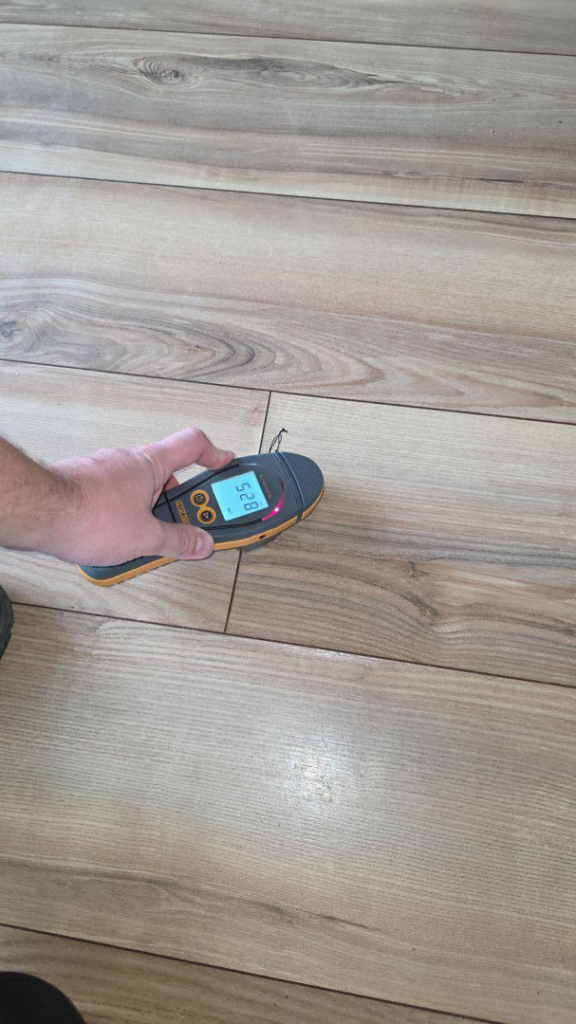 A hand using a moisture meter to detect moisture in wooden flooring at a job site for Restoration Techs, LLC in Oregon City, OR.