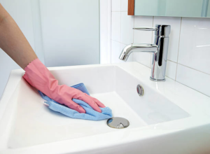 A gloved hand wiping a clean white bathroom sink with a blue cloth, demonstrating services by Clean Deeds in Olympia, WA.