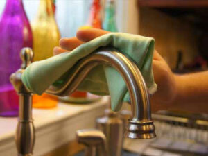 A hand meticulously wiping a kitchen faucet with a cloth, demonstrating attention to detail by Castle Keepers House Cleaning in North Charleston, SC.