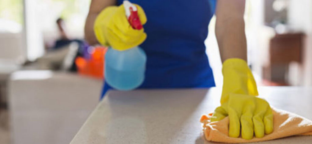 Gloved hands cleaning a bathroom sink with a spray bottle and yellow cloth, performed by Your Green Clean Crew in Bellevue, WA.