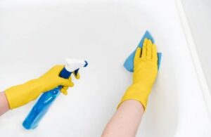 Hands in yellow gloves spraying cleaner and wiping a bathtub, showcasing cleaning services by Stella's Professional Cleaning LLC in Wilmington, NC.