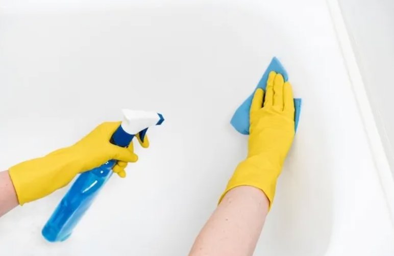 Hands in yellow gloves spraying cleaner and wiping a bathtub, showcasing cleaning services by Stella's Professional Cleaning LLC in Wilmington, NC.