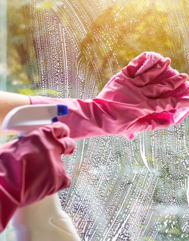Close-up of gloved hands spraying and wiping a window, demonstrating cleaning by Mid Atlantic Maid Service of Richmond, VA.