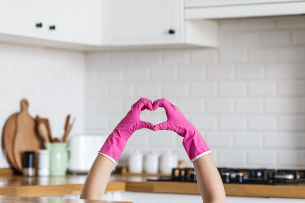 Hands in pink cleaning gloves forming a heart shape in a clean kitchen, symbolizing care from Christina's Tidy Homes in Canton, OH.
