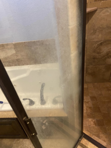 A shower door heavily stained with hard water and soap scum, ready for deep cleaning by Cleaning with Care in Fayetteville, AR.