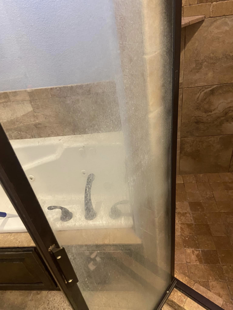 A shower door heavily stained with hard water and soap scum, ready for deep cleaning by Cleaning with Care in Fayetteville, AR.