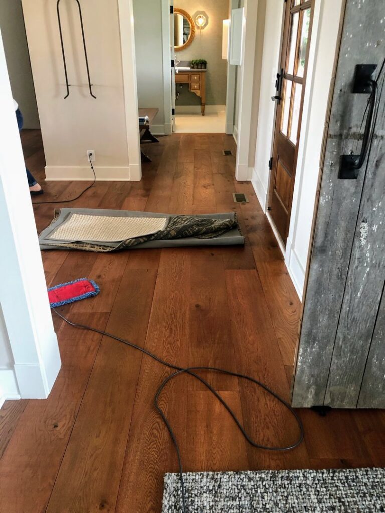 A hallway with hardwood floors being cleaned, showing a mop and vacuum cord from Price Cleaning Services Omaha in Council Bluffs, IA.