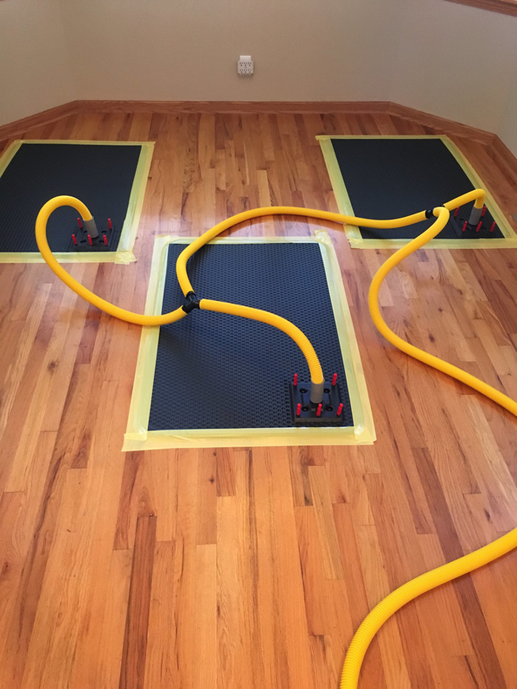 Specialized drying mats and hoses on a hardwood floor for water damage restoration by AllStar Response in Manhattan, KS