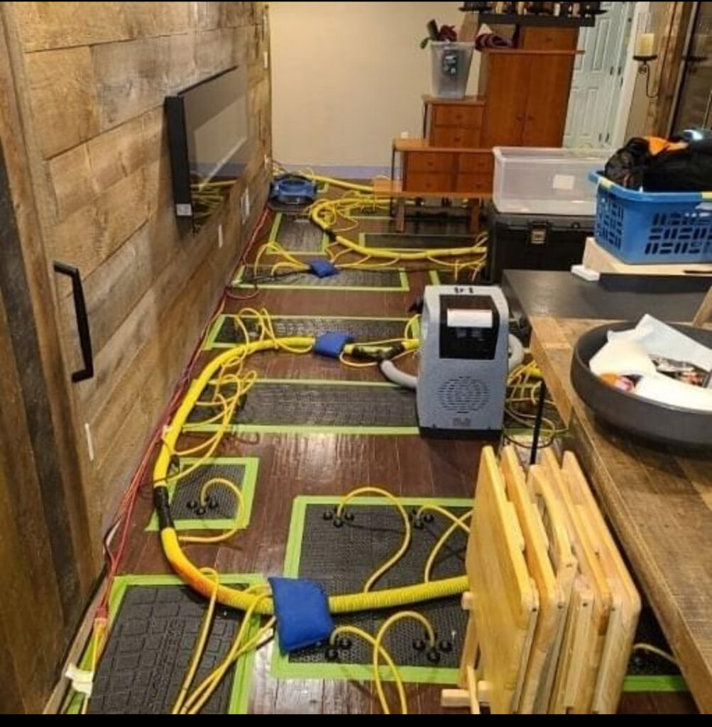 Hardwood floor drying mats and hoses connected to a dehumidifier for water damage restoration by New Method Restoration in Edison, NJ.