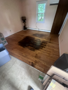 Severe water damage stain on a hardwood floor, indicating a need for restoration by PROTECH Restoration & Cleaning in Philadelphia, PA.