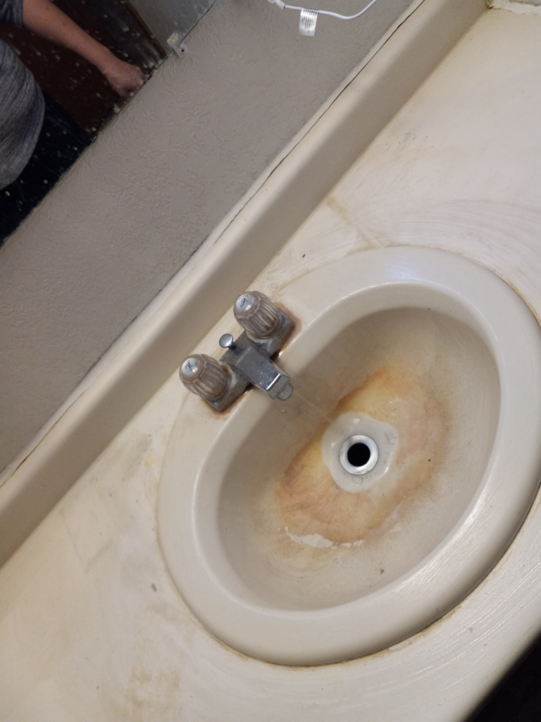 A heavily stained bathroom sink with rust and hard water marks, showing a cleaning task for J & A Cleaning and more in Norfolk, NE.