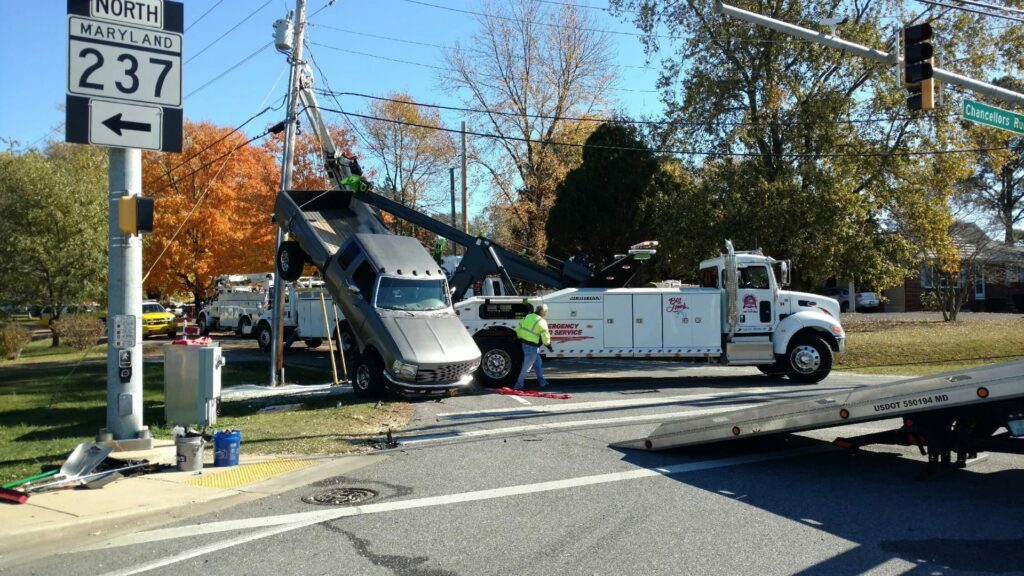 A heavy-duty wrecker recovering a grey pickup truck from an accident scene for Southern Maryland Towing in Prince Frederick, MD.