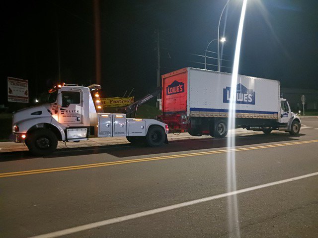 An Elite Towing of Minnesota heavy-duty tow truck towing a Lowe's box truck at night in St Paul, MN.