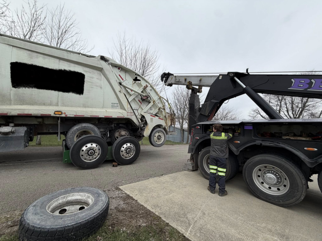 A heavy-duty tow truck from Bevis Towing lifting a large garbage truck during a recovery job in Cincinnati, OH.