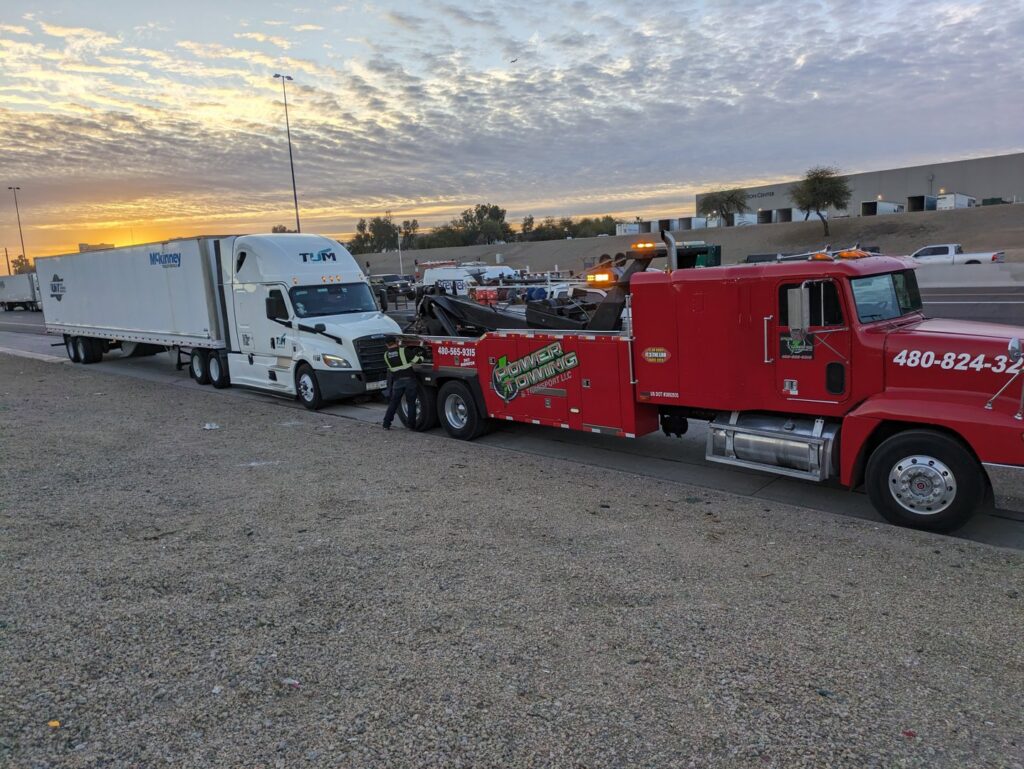 A red heavy-duty tow truck from Power Towing & Transport preparing to tow a semi-truck with a trailer on a highway in Phoenix, AZ.