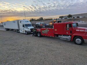 A red heavy-duty tow truck from Power Towing & Transport preparing to tow a semi-truck with a trailer on a highway in Phoenix, AZ.