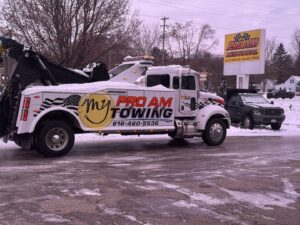 A heavy-duty tow truck with Pro Am Towing branding parked in a snowy lot at Pro Am Collision & Mechanical in Grand Rapids, MI.