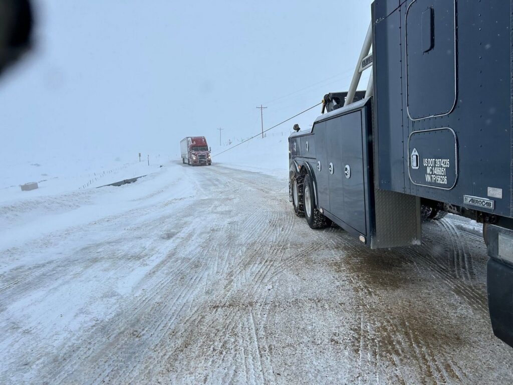 A heavy-duty tow truck from Select Towing and Recovery pulling a semi-truck on a snowy road in Casper, WY.