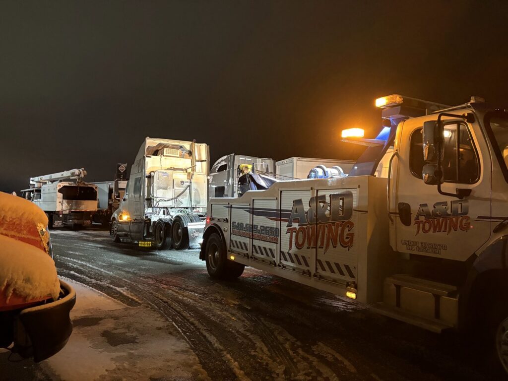 A heavy-duty tow truck from A and D Towing is recovering multiple semi-trucks on a snowy night in Little Ferry, NJ.