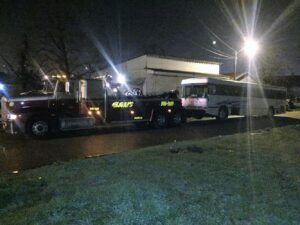 A heavy-duty tow truck from Glenn's Towing & Recovery Inc towing a large white bus at night in Lafayette, LA.