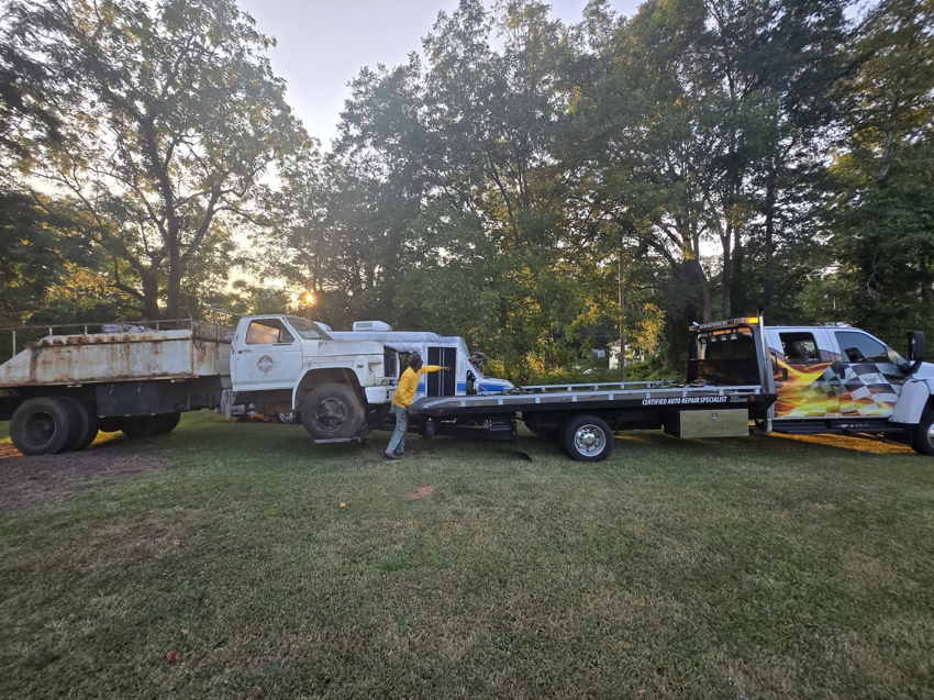 A heavy-duty tow truck from Dees Custom Auto towing an older dump truck in Newnan, GA.