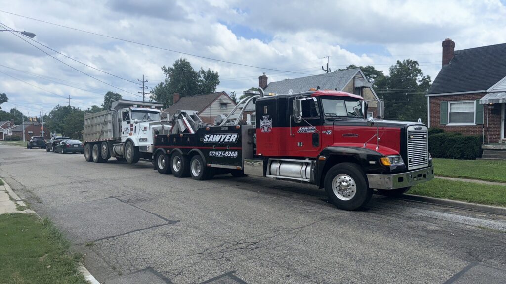 A heavy-duty tow truck from Sawyer Towing is actively towing a large dump truck in Cincinnati, OH.