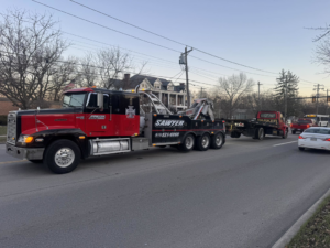 A heavy-duty tow truck from Sawyer Towing is towing a smaller flatbed tow truck on a street in Cincinnati, OH.