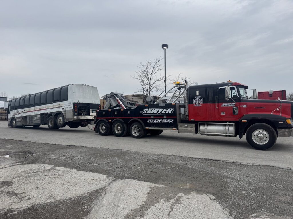 A heavy-duty tow truck from Sawyer Towing is actively towing a large passenger bus in Cincinnati, OH.