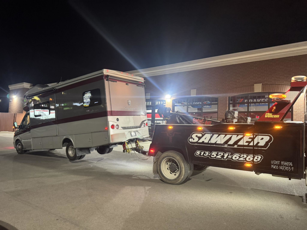 A heavy-duty tow truck from Sawyer Towing is actively towing an RV or motorhome at night in Cincinnati, OH.