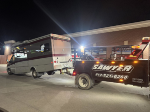A heavy-duty tow truck from Sawyer Towing is actively towing an RV or motorhome at night in Cincinnati, OH.